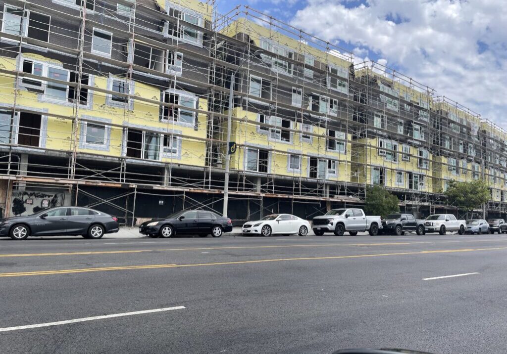 A building under construction with cars parked on the side of it.